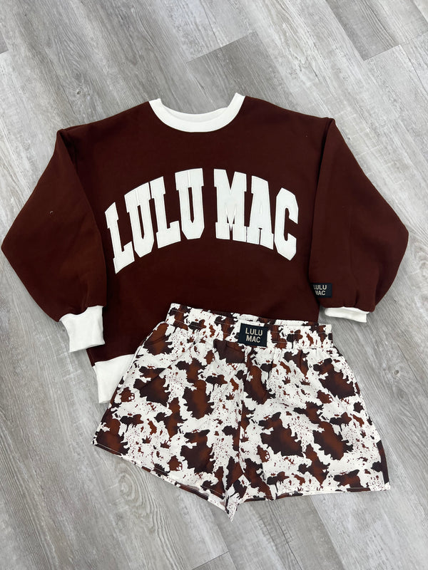 Brown hoodie with white text and patterned shorts on a wooden floor