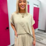 Woman in beige outfit standing in a hallway with pink lockers.