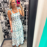 Woman taking a mirror selfie wearing a floral dress in a room with a patterned wall.