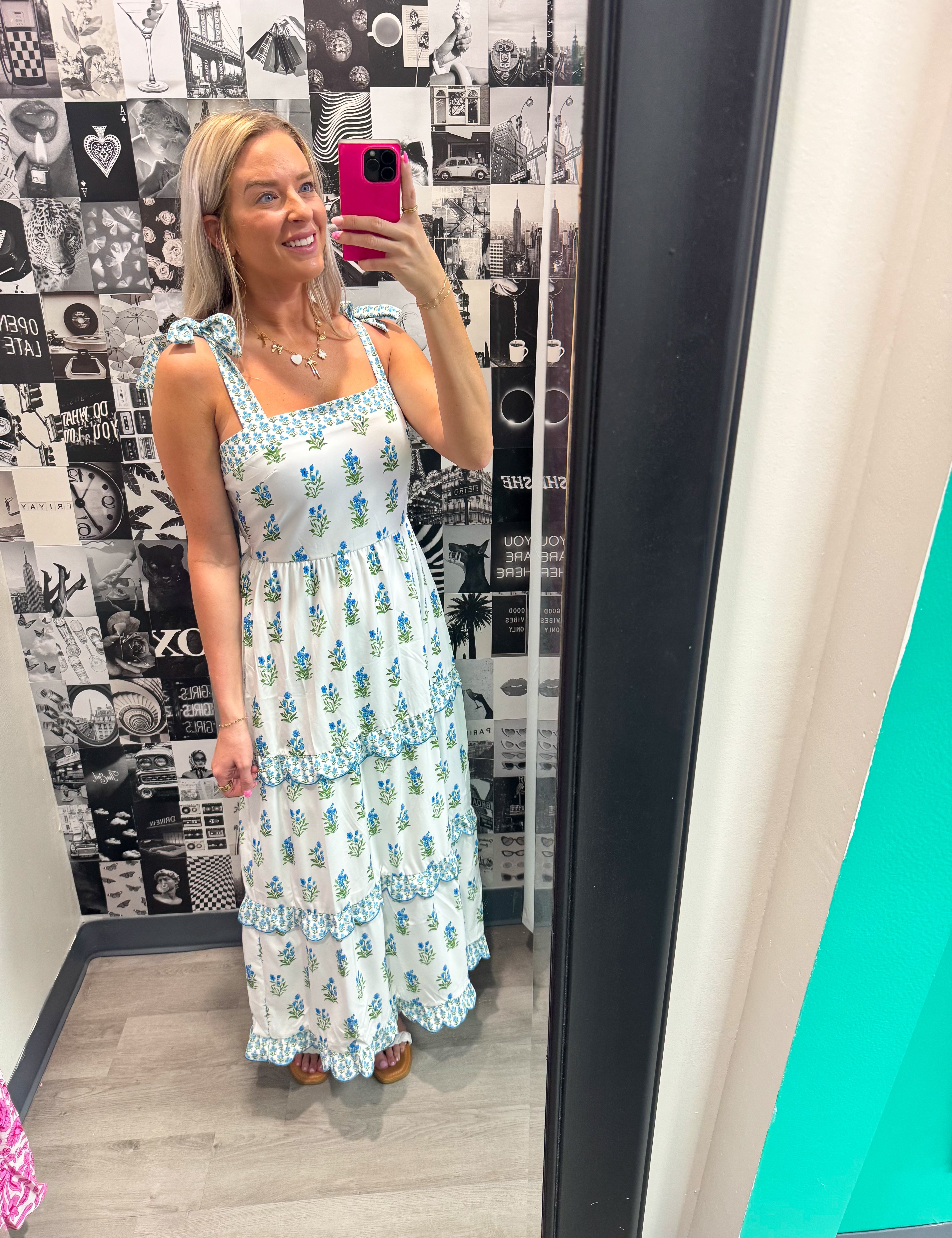 Woman taking a mirror selfie wearing a floral dress in a room with a patterned wall.