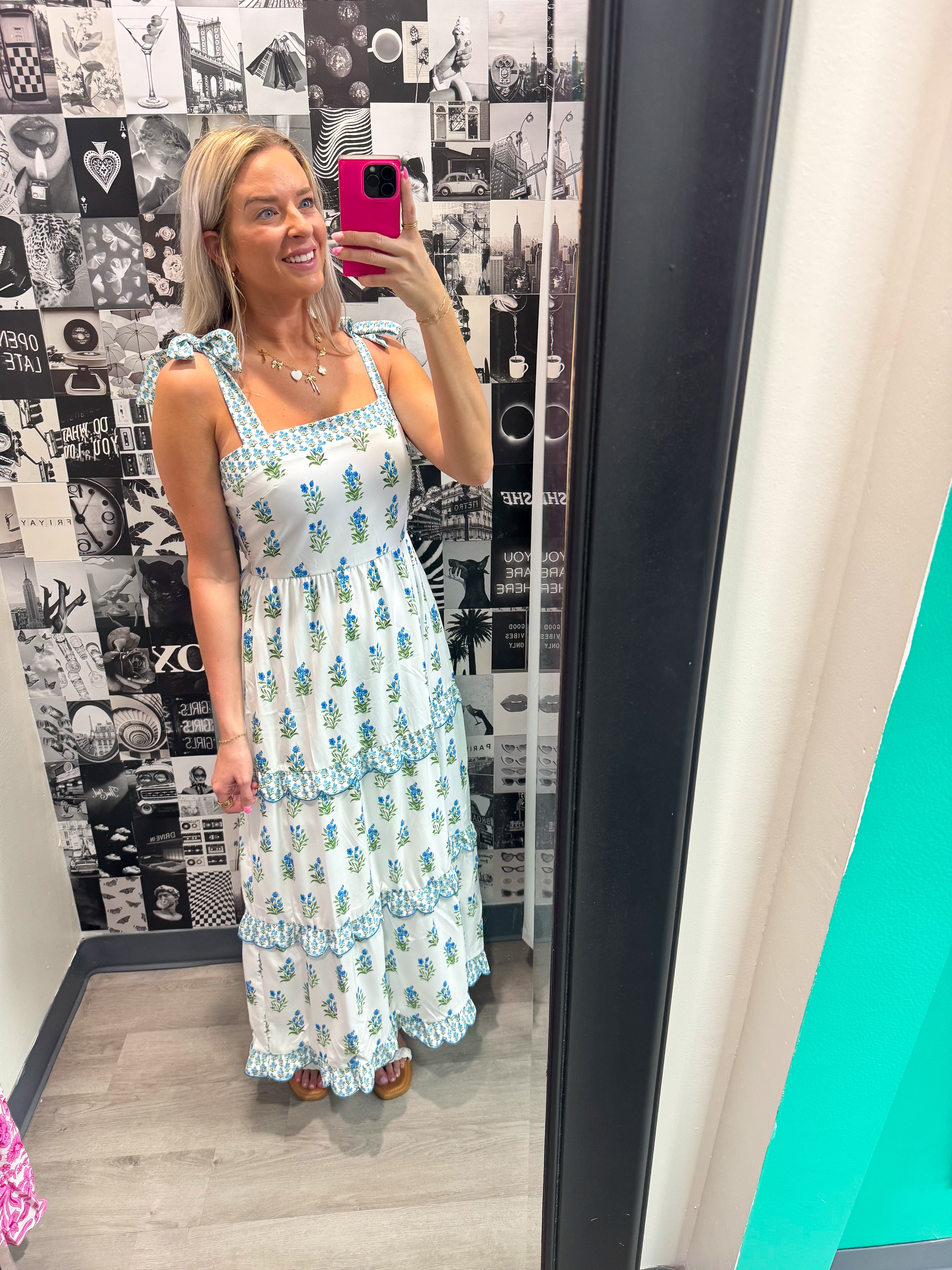 Woman taking a mirror selfie wearing a floral dress in a room with a patterned wall.