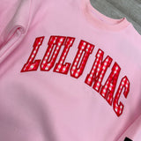 Pink sweatshirt with red 'LULU MAE' text on a gray surface