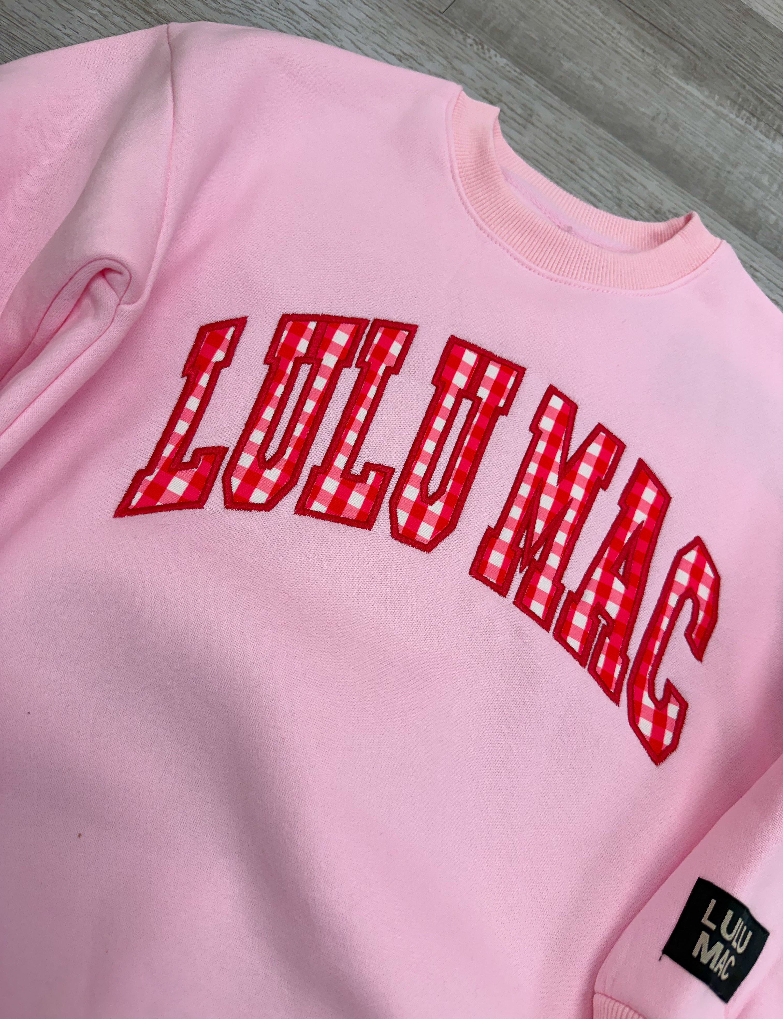 Pink sweatshirt with red 'LULU MAE' text on a gray surface