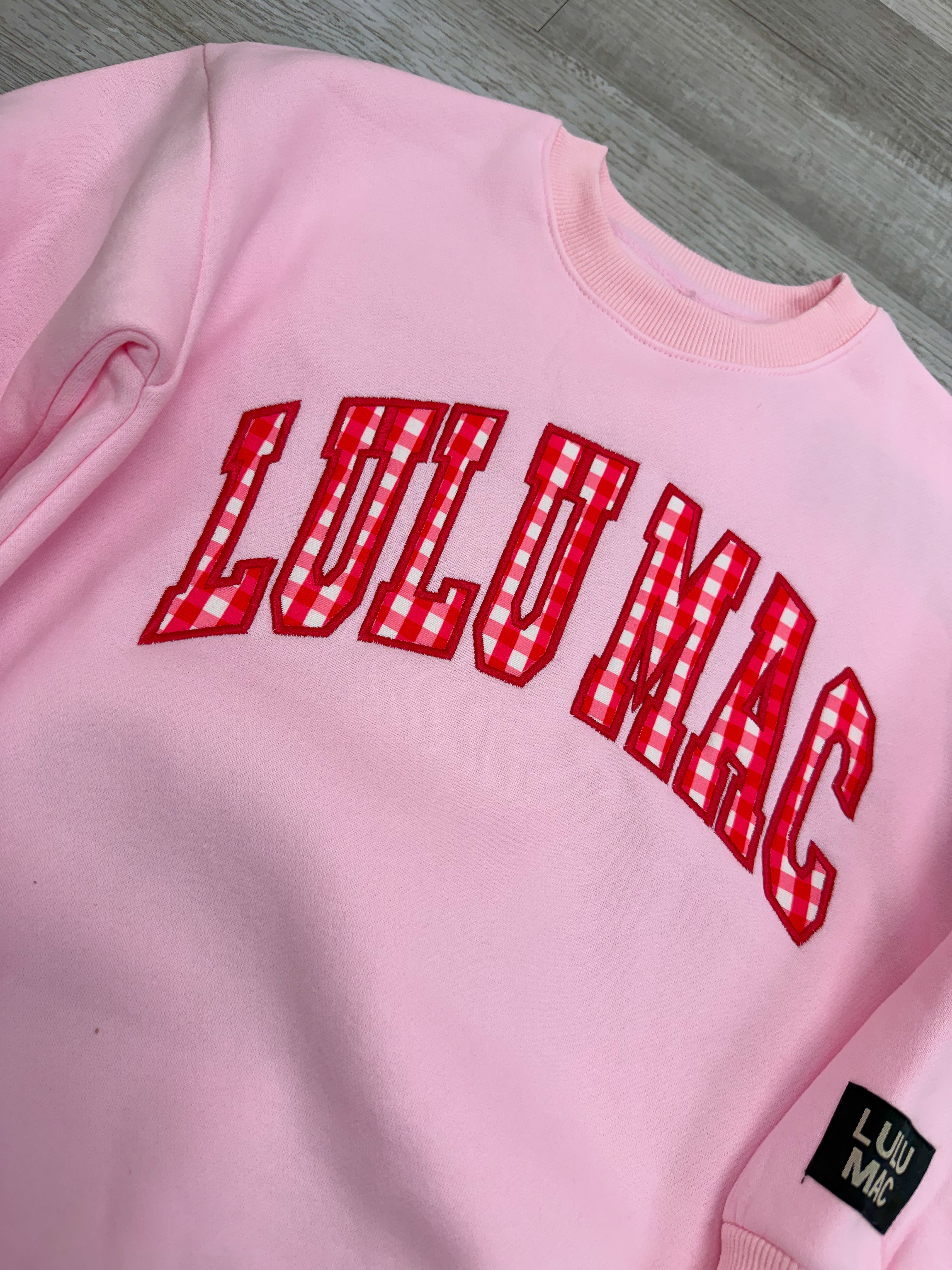 Pink sweatshirt with red 'LULU MAE' text on a gray surface