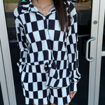 Woman wearing a black and white checkered outfit standing in front of a store entrance.