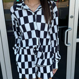 Woman wearing a black and white checkered outfit standing in front of a store entrance.