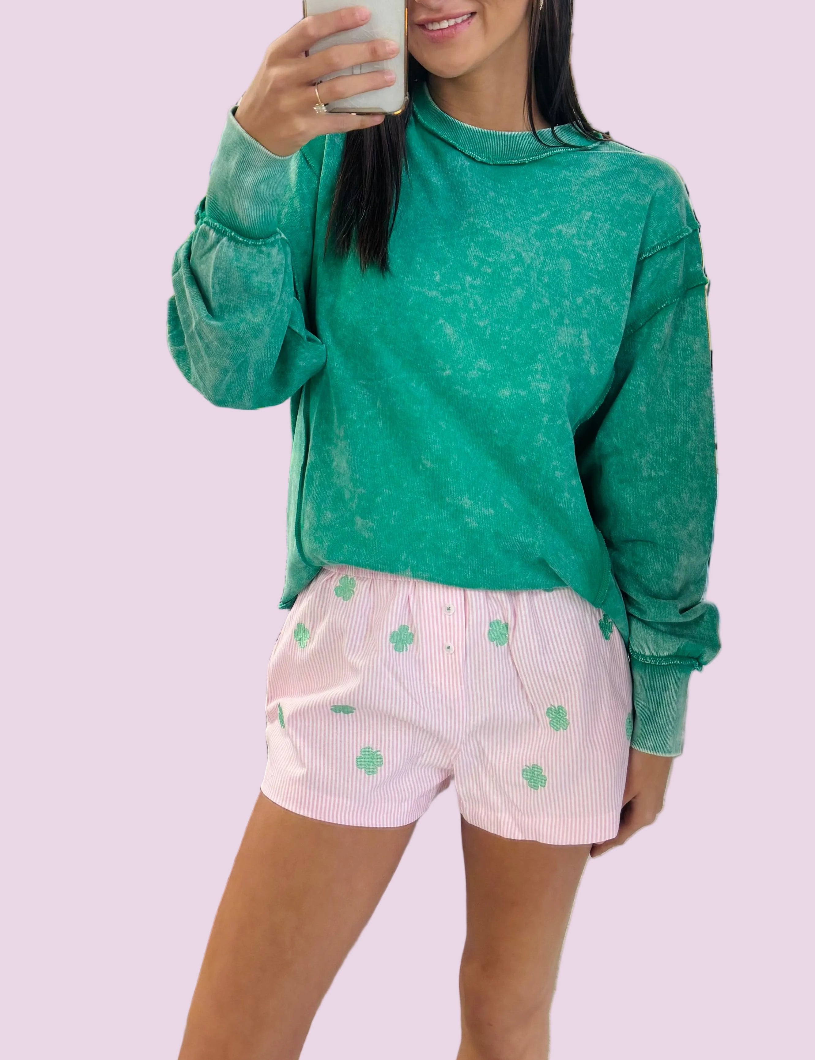 Person taking a mirror selfie wearing a green sweatshirt and pink shorts with white patterns in a store.