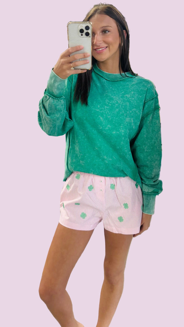 Person taking a mirror selfie wearing a green sweatshirt and pink shorts with white patterns in a store.
