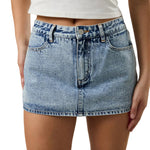 Person wearing a light blue denim skirt on a neutral background