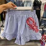 Striped shirt with red lobster design held by a hand in a store setting