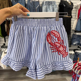 Striped shirt with red lobster design held by a hand in a store setting