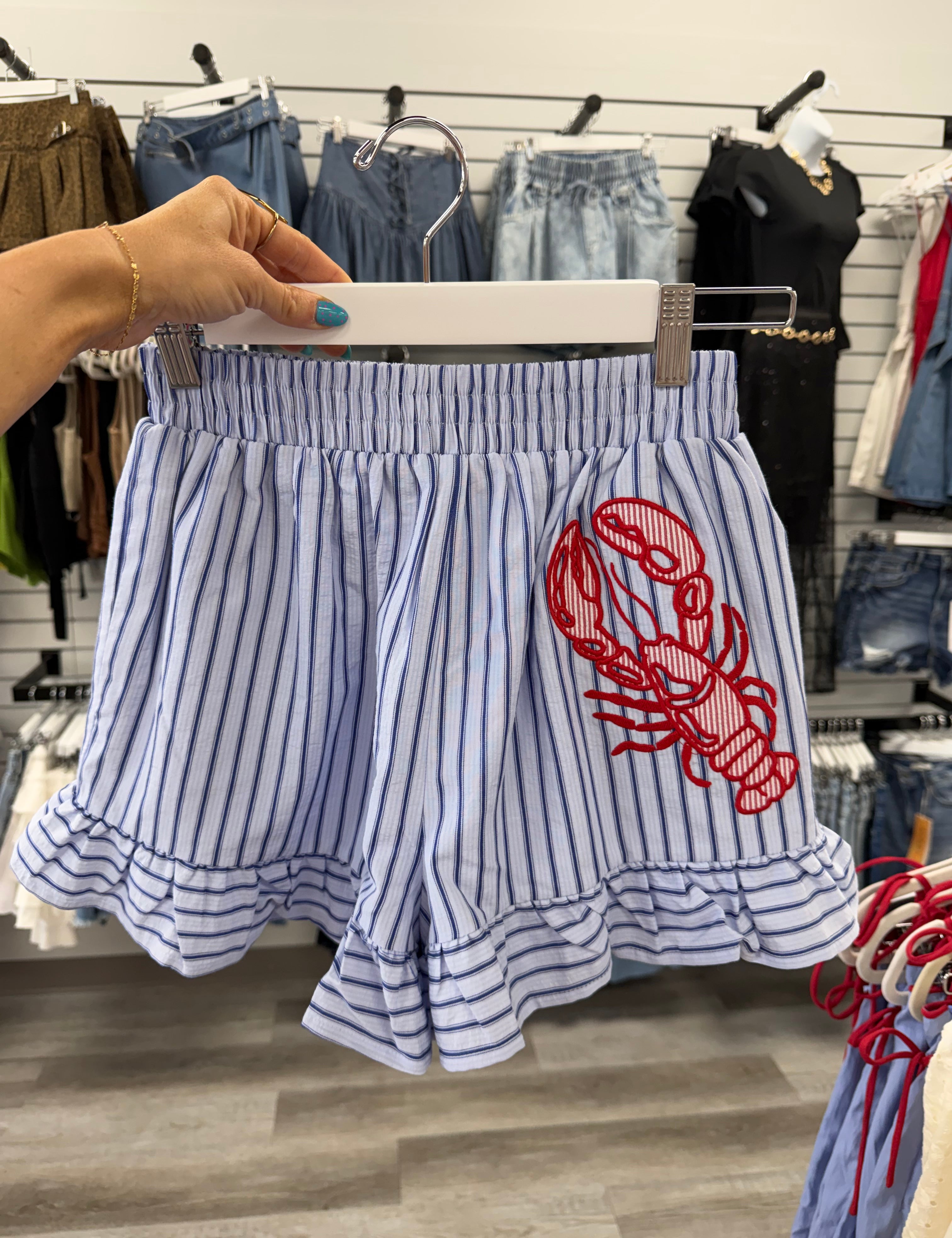 Striped shirt with red lobster design held by a hand in a store setting