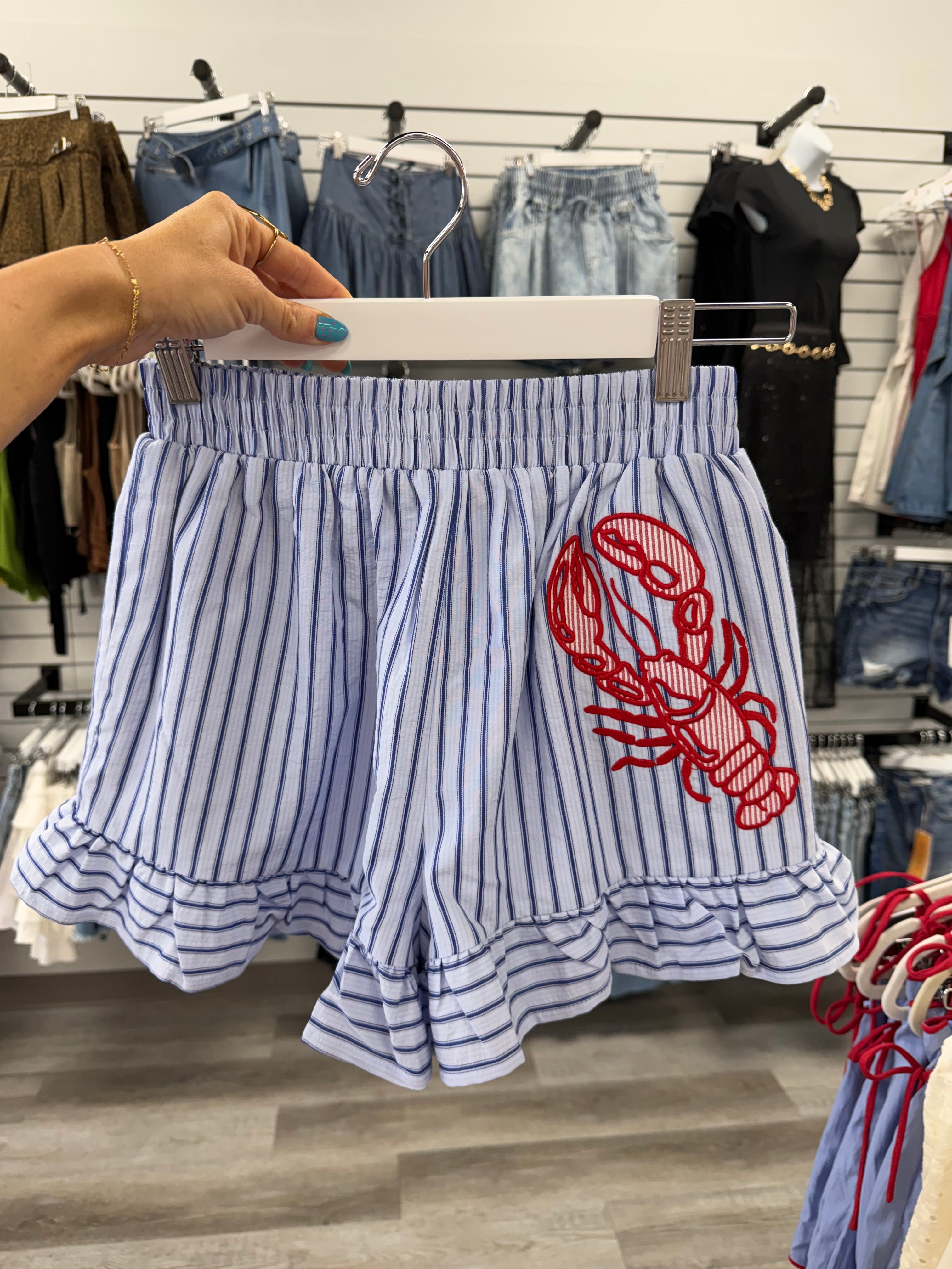 Striped shirt with red lobster design held by a hand in a store setting