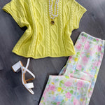Yellow cable knit top with floral pants and white heels on a gray surface