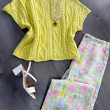 Yellow cable knit top with floral pants and white heels on a gray surface