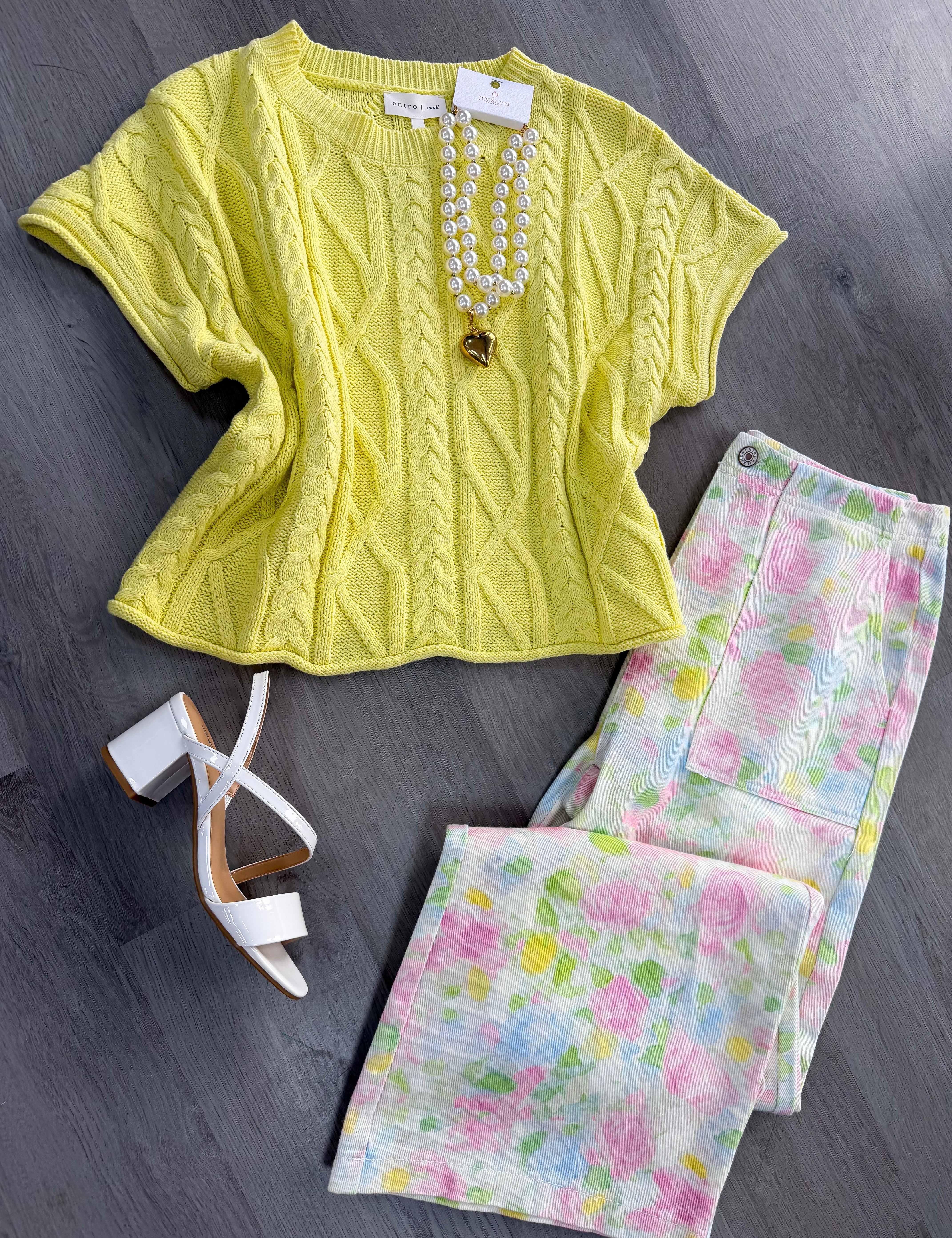 Yellow cable knit top with floral pants and white heels on a gray surface