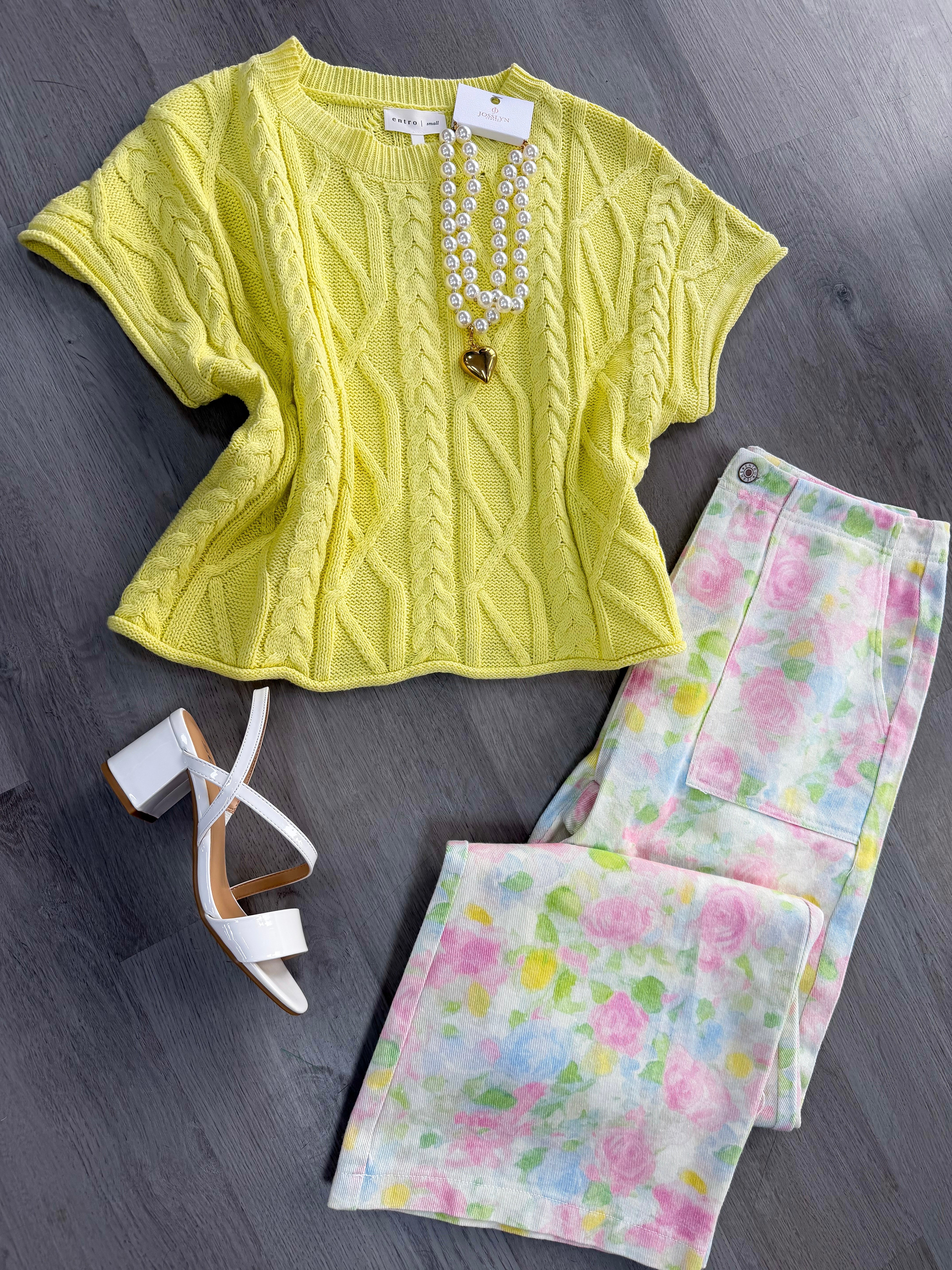 Yellow cable knit top with floral pants and white heels on a gray surface