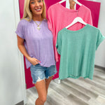 Woman holding two shirts, one pink and one green, in a store setting.