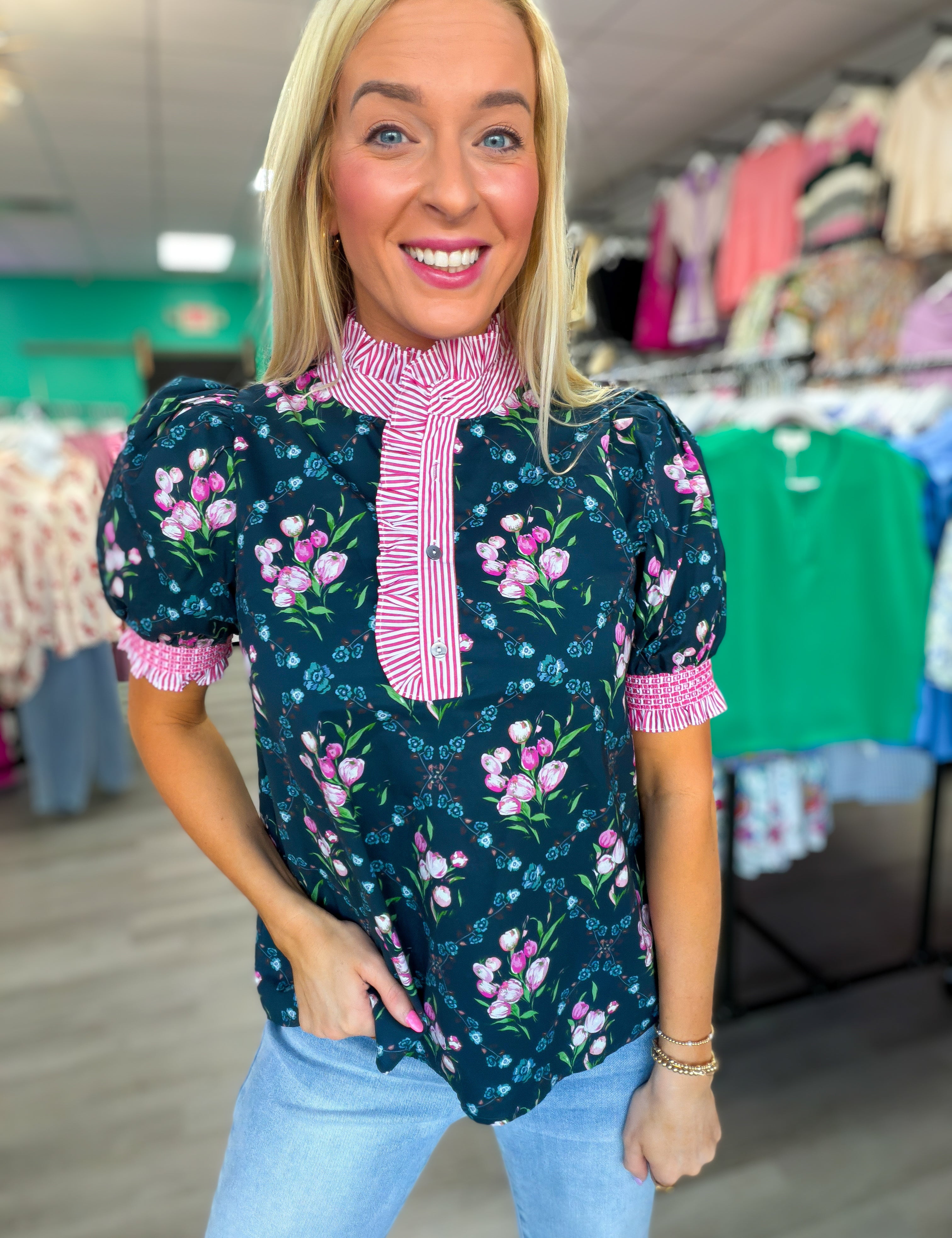 Woman wearing a floral blouse with pink trim in a clothing store.