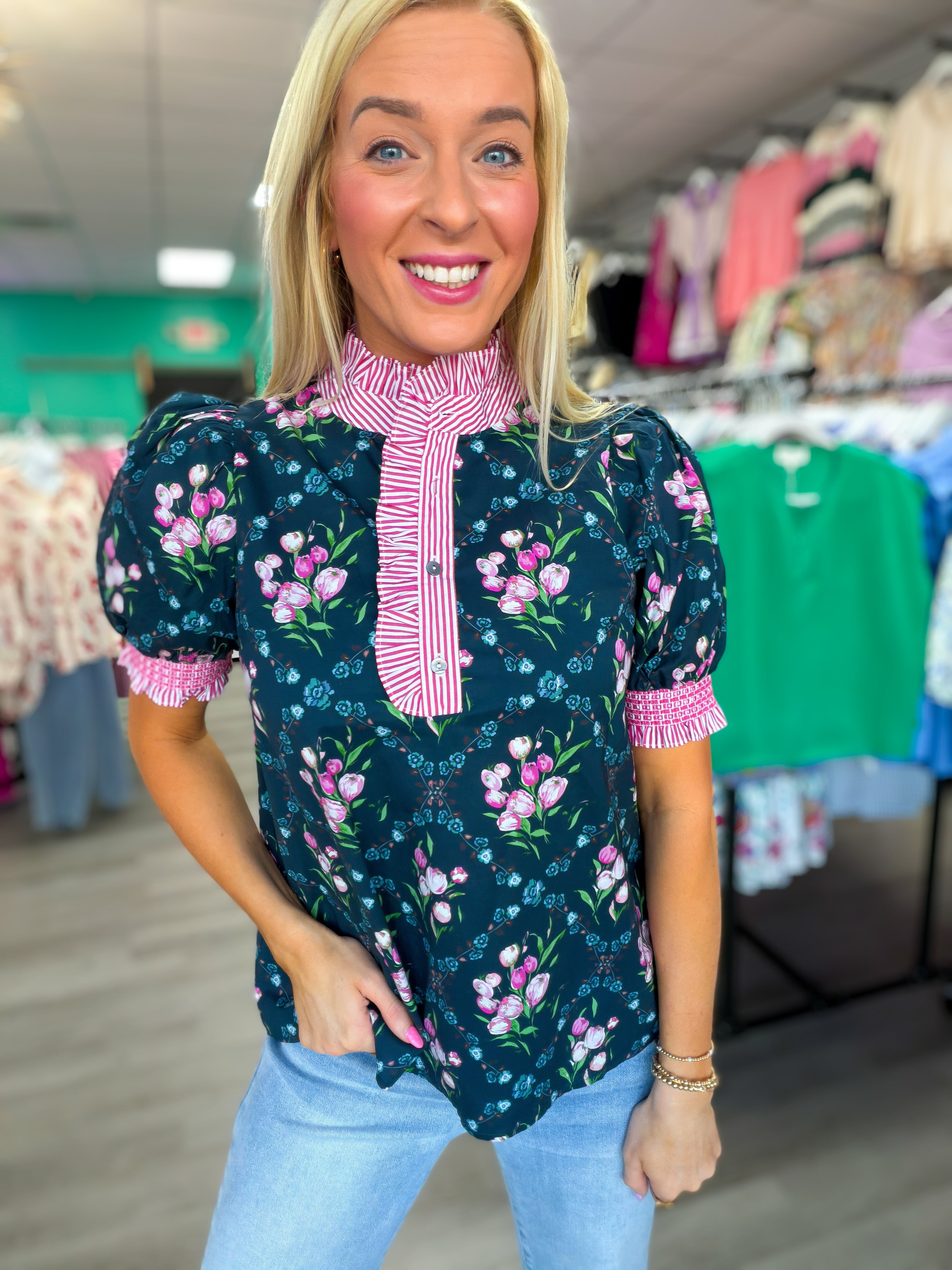Woman wearing a floral blouse with pink trim in a clothing store.