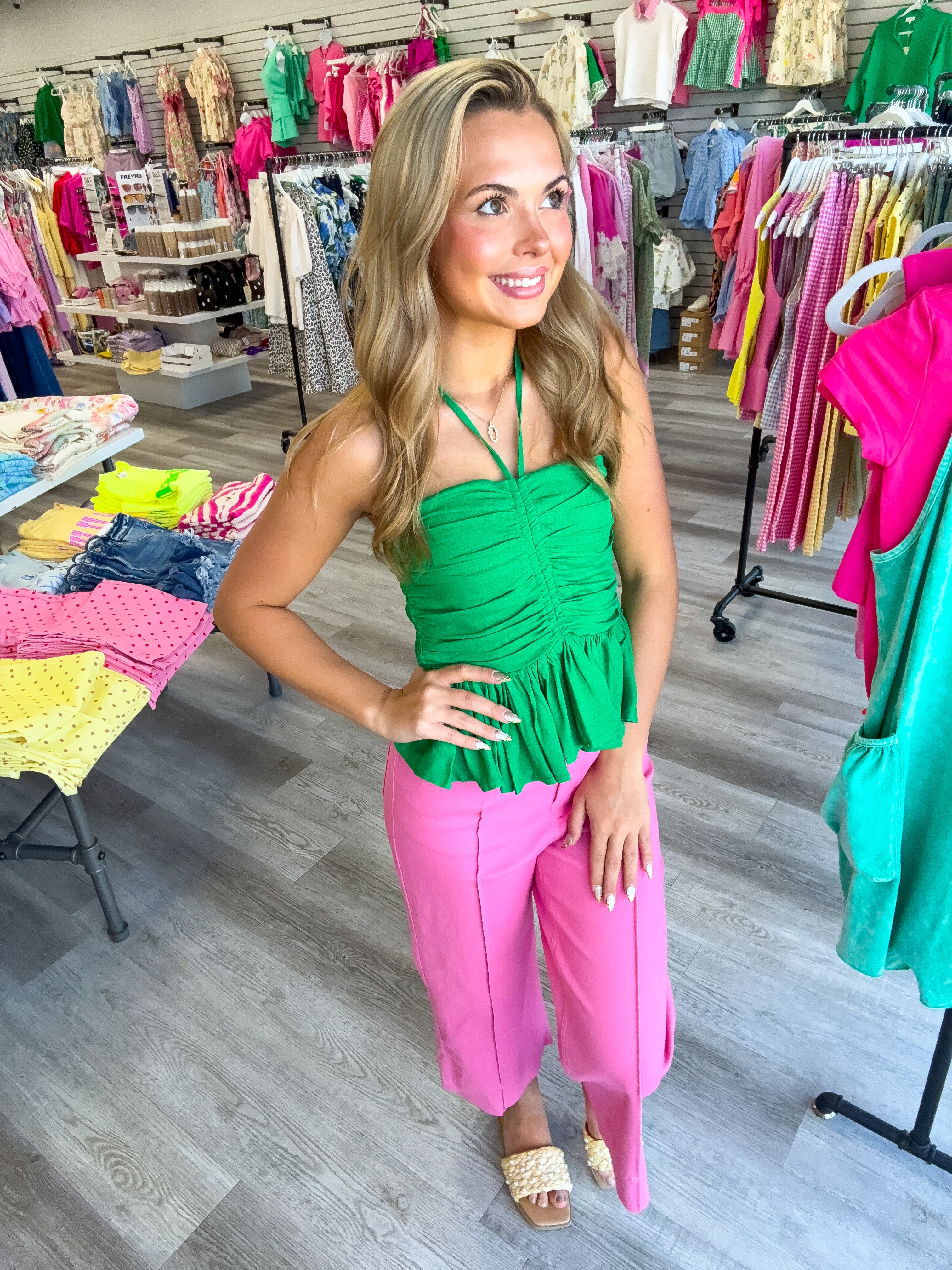 Woman in a green top and pink pants standing in a colorful clothing store.