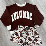 Brown hoodie with white text and patterned shorts on a wooden floor