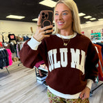Woman wearing a brown sweatshirt with 'SULU MIA' text in a store setting