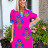 Woman wearing a bright pink dress with blue floral patterns standing in front of a house.