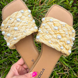 Beige sandals with pearl embellishments held on grass