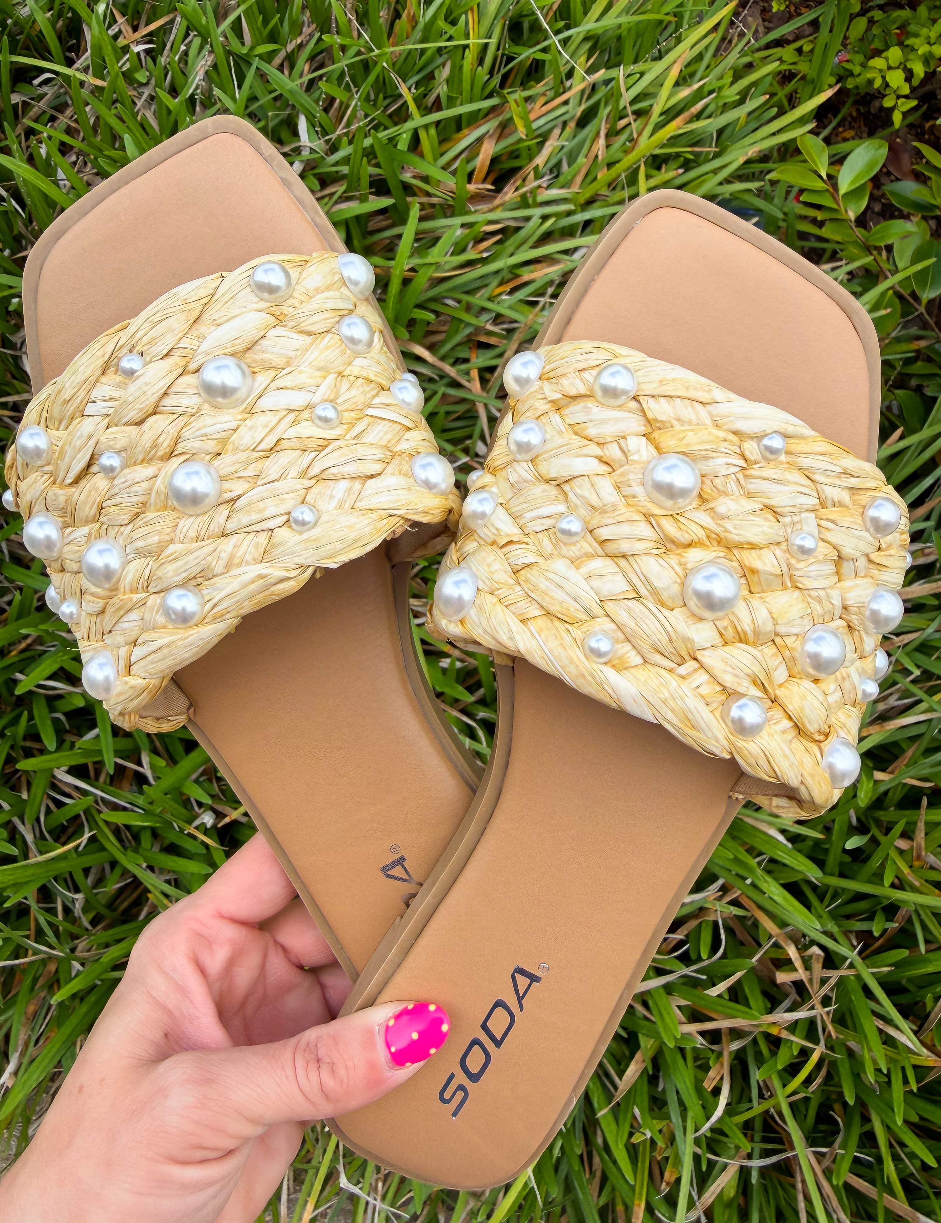 Beige sandals with pearl embellishments held on grass