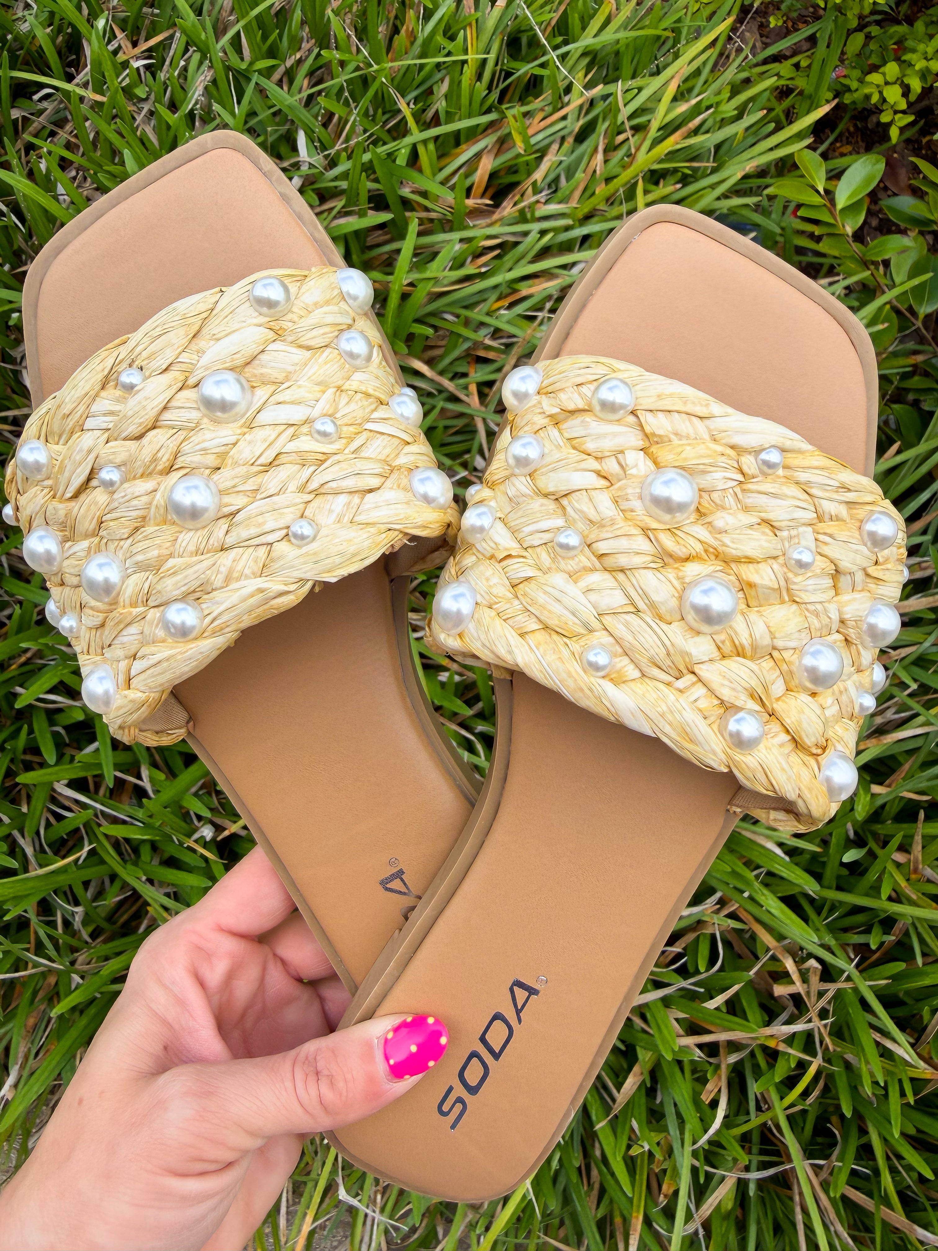 Beige sandals with pearl embellishments held on grass