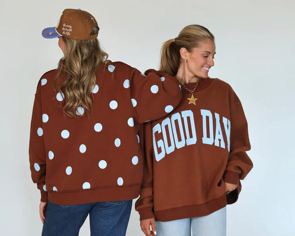 Two people wearing brown sweatshirts with polka dots and 'GOOD DAY' text, standing back-to-back against a white background.