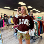 Person wearing a maroon sweatshirt with 'LULU MAC' printed on it in a clothing store.