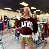 Person wearing a maroon sweatshirt with 'LULU MAC' printed on it in a clothing store.