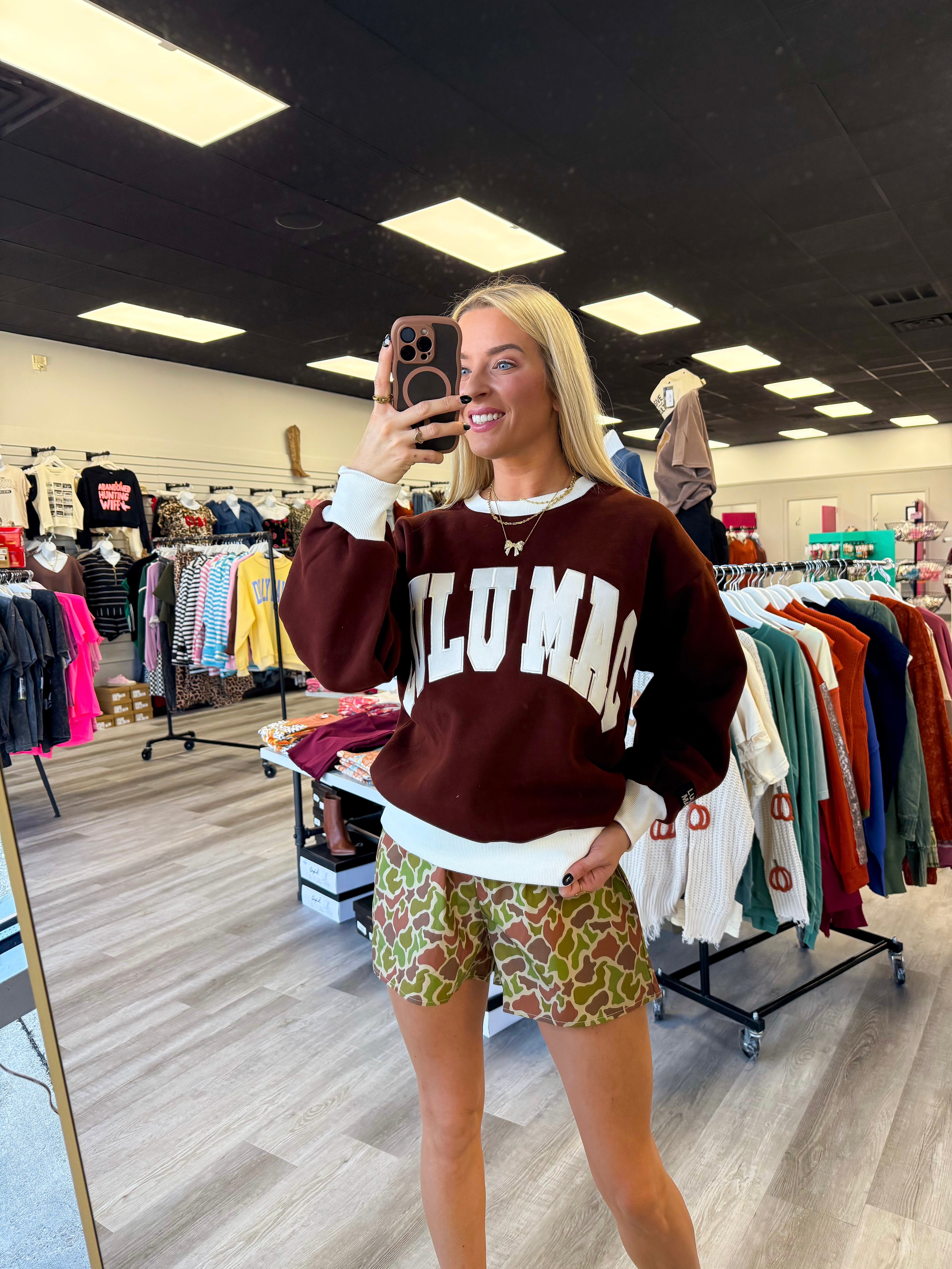 Person wearing a maroon sweatshirt with 'LULU MAC' printed on it in a clothing store.