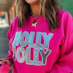 Person wearing a pink sweatshirt with 'Holly Jolly' text, holding colorful pom-poms.